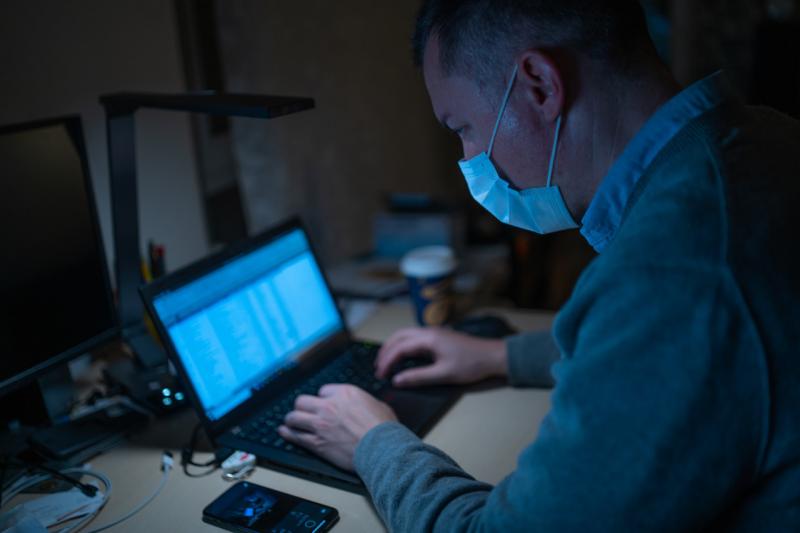 Мужчина работает за ноутбуком в защитной медицинской маске