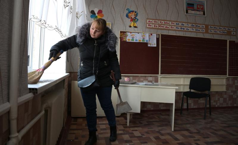 Женщина убирает осколки окон поврежденного в результате обстрела здания школы