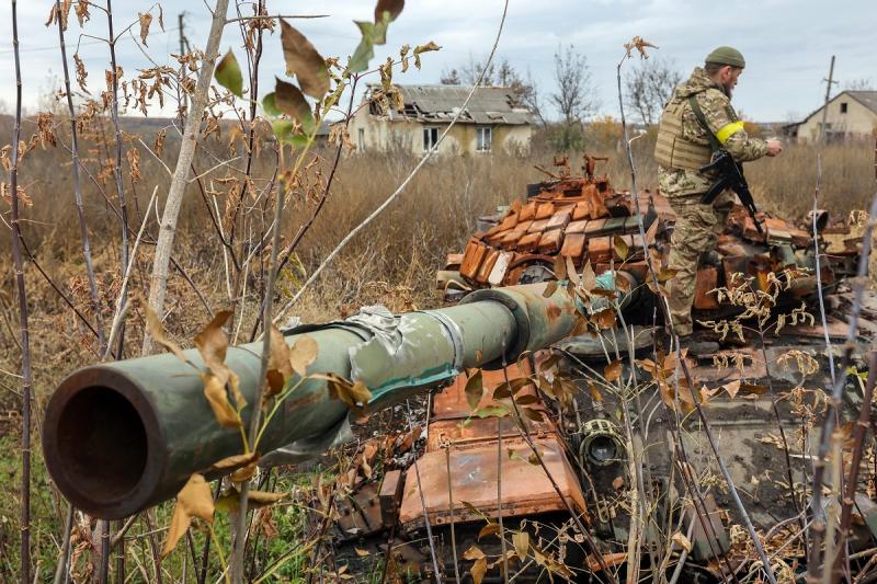 украинский военный рядом с подбитым русским танком