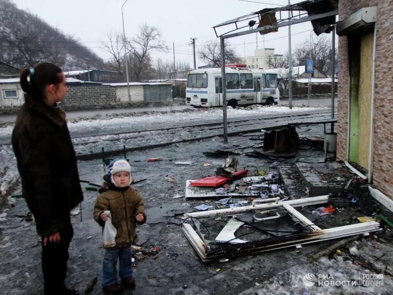 Женщина с ребенком на фоне разрушенного здания в Донбассе
