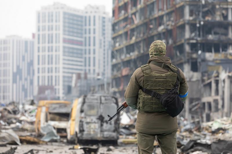 украинский военный на фоне разрушенного дома