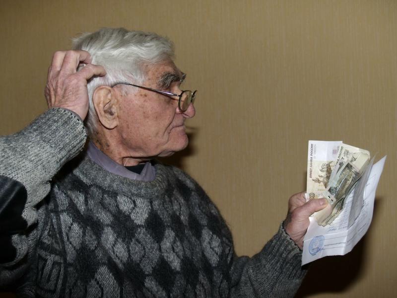 пенсионер смотрит на квитанцию и чешет затылок, так как в шоке от сумм