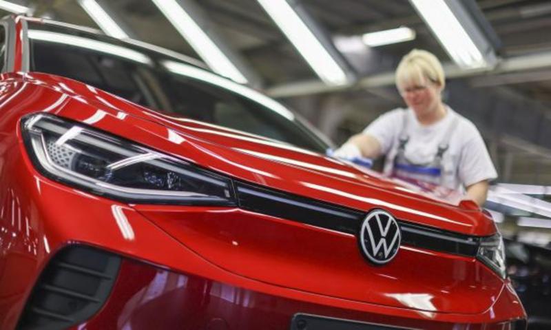 Женщина-сотрудница автоконцерна Volkswagen полирует кузов красного автомобиля на заводе
