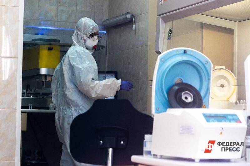 Женщина-врач в защитном костюме для работы с инфекциями, маске и очках стоит у аппарата для анализов
