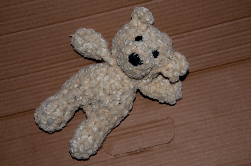 Мягкая игрушка в виде медвежонка серо-бежевого цвета лежит на столе