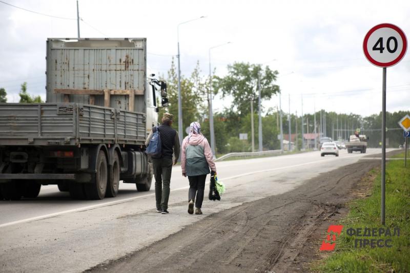 Мужчина и женщина в весенней одежде идут по обочине сельской дороги, рядом едет грузовик