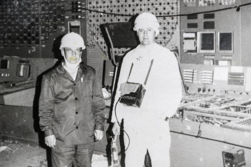 Двое ликвидаторов чернобыльской аварии в касках стоят на фоне пульта управления атомный станции