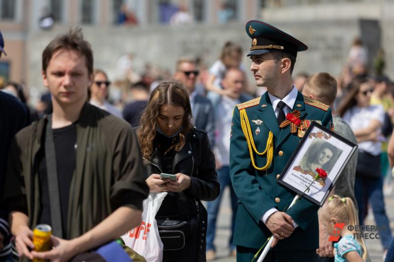 Военный слева стоит с портретом ветерана в колонне Бессмертного полка, в центре девушка