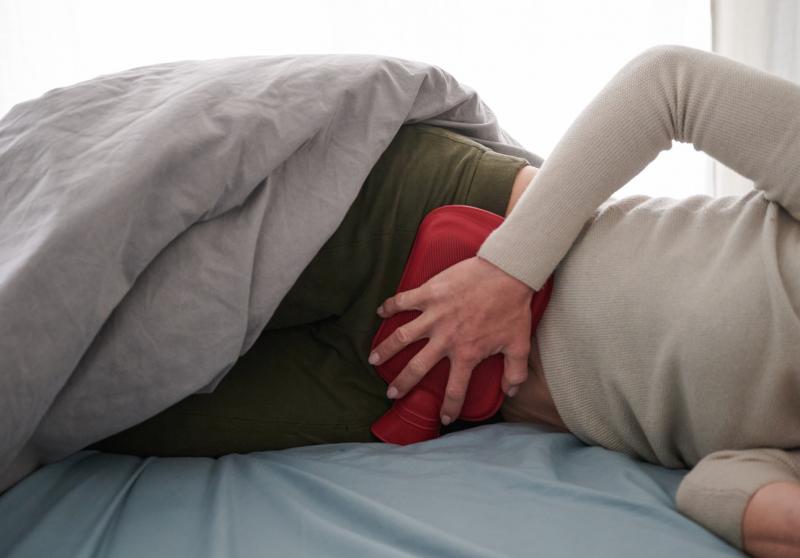 Женщина лежит под одеялом с грелкой на животе