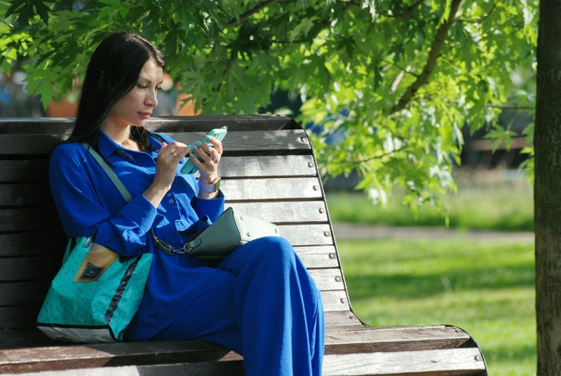 Женщина со смартфоном на скамейке в парке