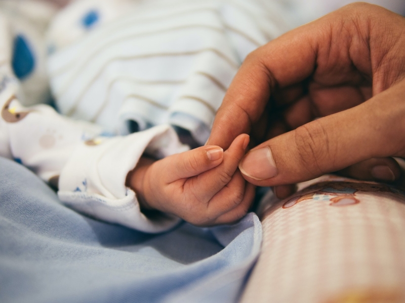 Взрослый держит за руку младенца в больнице