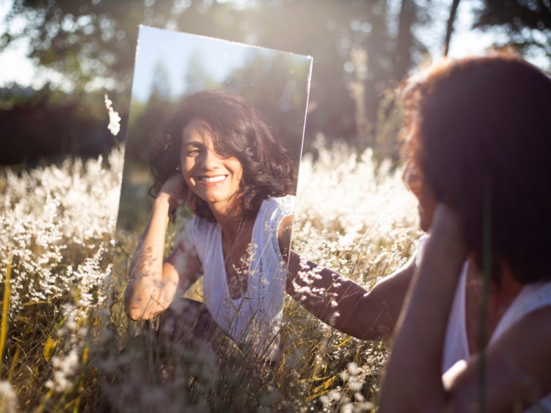 Девушка смотрится в зеркало в открытом поле