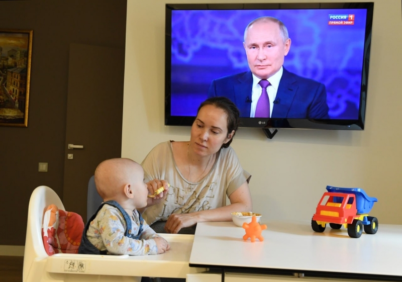 Женщина кормит сына на фоне выступления Путина