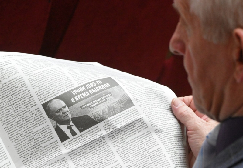 Участник съезда КПРФ читает партийную газету с фотографией Геннадия Зюганова