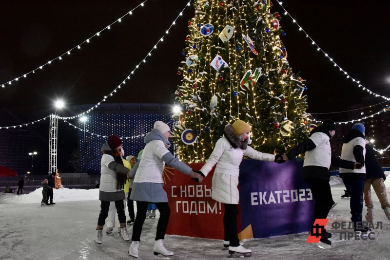 Молодые люди катаются на коньках вокруг новогодней елки
