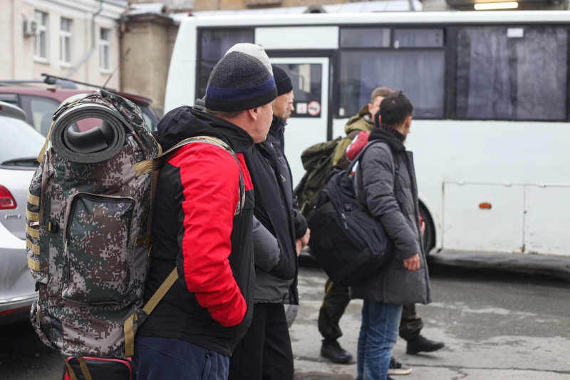 Мужчины стоят с рюкзаками возле автобусов