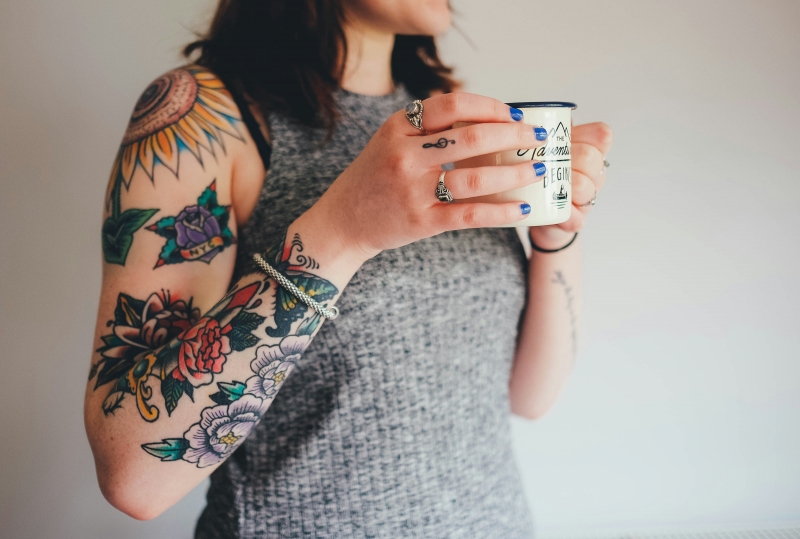 Девушка с татуировками держит кружку